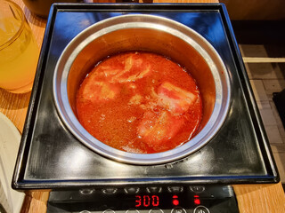 A close-up of a hot pot filled with spicy red soup and tofu cubes, placed on an induction cooker, ready for cooking