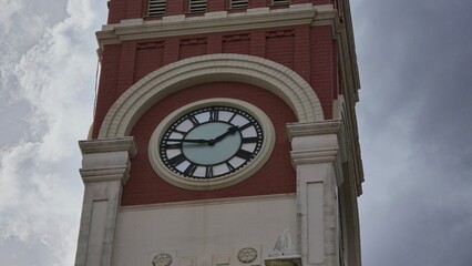 Close-up of a historic clock tower with red brick and white stone detailing, showcasing its ornate...