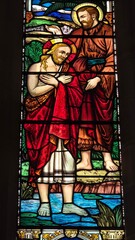 Fototapeta premium Stained-glass depiction of Jesus' baptism, with John the Baptist pouring water over Him. Rich details include vibrant reds and greens, a flowing river, and a serene countryside background.