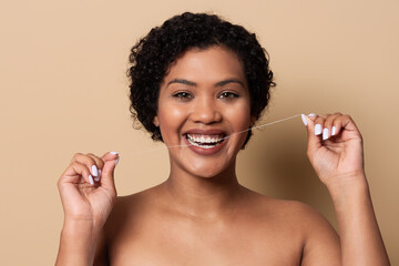 A woman with curly hair is smiling widely while holding dental floss. She demonstrates proper...