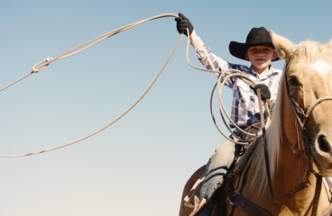 Western industry with young cowboy horseback on palomino closeup swinging rope in air, copy space...