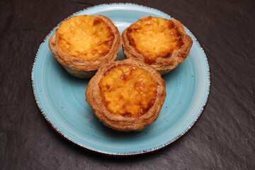 Custard egg tart caramelized stuffed flaky buttery puff pastry on blue plate over black slate