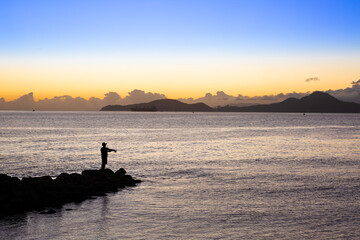 Lone fisherman fishing on the rocks at Ponta da Praia, in Santos, during sunset