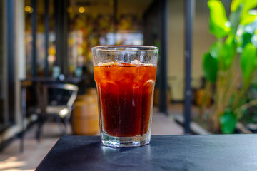 An iced americano served on a table at a coffee shop, with a cozy cafe ambience in the background. The cool beverage adds to the relaxed atmosphere of the cafe setting