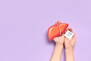 Female hands with paper liver and sad smile on lilac background