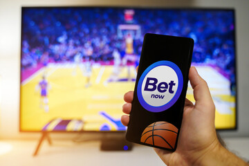 Betting app on mobile phone, live match betting concept for basketball games. Man hand holding smartphone in front of tv screen