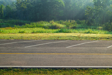 Empty parking lot against meadow and beautiful forest with light in morning.