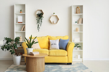 Interior of stylish room with comfortable yellow sofa, coffee table and shelving units