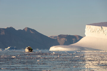 small tourist boat next to a huge iceberg in polar regions, Greenland