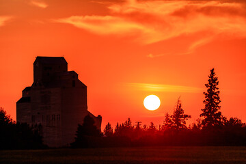 A large building with a tower is silhouetted against the orange sky