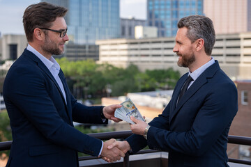 Fototapeta premium Businessmen shaking hands and receiving banknote. Businessman giving money outdoor. Receiving money. Bills money,finance staff counting money, finance, saving, banking, and people concept.