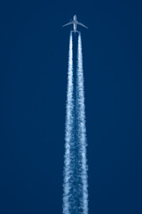 Passenger jet flies overhead with jet stream portrait view with deep blue sky background.