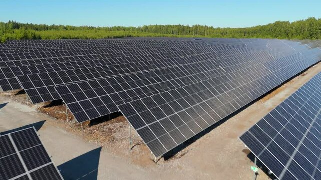 Aerial angled fast dolly of bifacial panels at Solar Farm with glistening sunlight amongst green trees