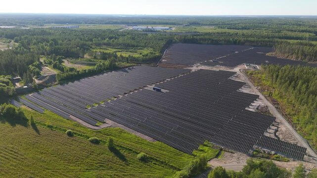 High angle panoramic overview of rows of bifacial solar panels at productiong area in middle of forest and field