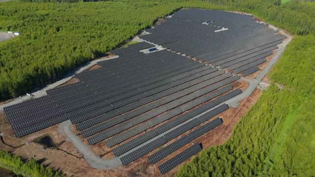Broad aerial sweep over bifacial panels of Solar Farm in Finland showcasing energy production with reflection fading as drone orbits