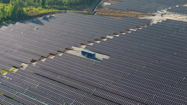 Aerial drone orbit of Solar Farm's bifacial solar panels producing energy in Finland with container office structure in center