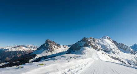 Obraz premium Snowy mountain landscape with a ski slope, offering a winter wonderland and clear blue sky.