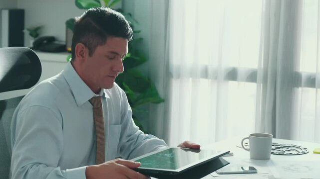 Professional engineer looking at phone while working on tablet with green screen at meeting table with turbine engine or jet engine sketch design and various metal gear scatter around. Alimentation.