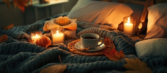 Cozy autumn scene with a steaming coffee cup and candles creating a warm atmosphere on a bed surrounded by decorative leaves and pumpkins