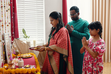 Obraz premium Family participating in traditional cultural ritual, standing in prayer. Family members are dressed in colorful attire, with offerings and decorative items on altar table