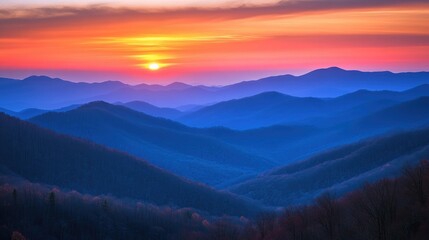 Fototapeta premium Serene mountain vista bathed in vibrant sunset hues, showcasing layers of blue ridges and a glowing orange sky.