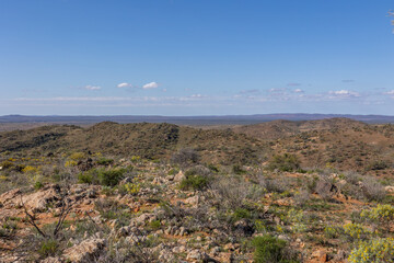 A rocky and low hill landscape with sparse vegetation under a blue sky with clouds in the semi arid area around Broken Hill in New South Wales, Australia.