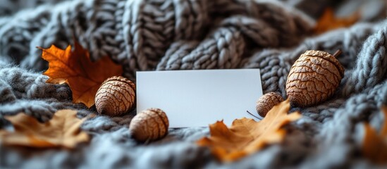 Obraz premium Blank card mockup on a cozy knitted blanket surrounded by autumn leaves and acorns, perfect for seasonal greetings or invitations.