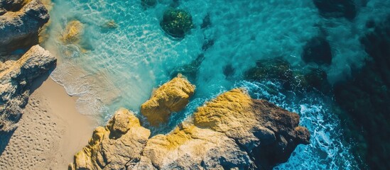 Aerial view of pristine coastline with crystal clear blue water and vibrant yellow rocks beside sandy beach.