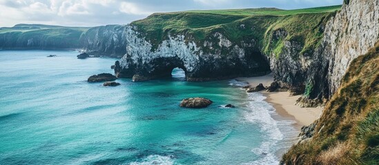 Fototapeta premium Breathtaking coastal landscape with turquoise waters and dramatic cliffs meeting a sandy beach under a cloudy sky