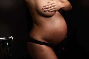 Faceless pregnant woman getting an instant tan. The master applies bronzer with a spray.