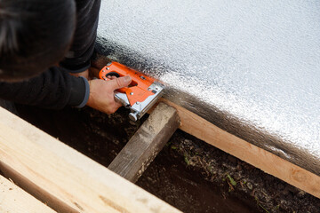 A man is using a staple gun to attach a piece of insulation to a wooden board