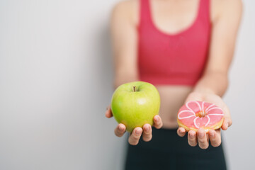woman hand hold green Apple and donut, female fitness choose between fruit is Healthy and sweet is Unhealthy junk food. Dieting control, Weight loss, Obesity, eating lifestyle and nutrition concept