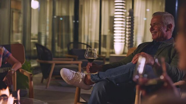 Woman drinks wine with friends around a fire pit in a luxury outdoor area