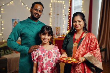 Family posing in decorated home during Diwali celebration Holding a decorated plate with lights and...