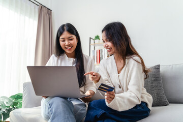 Fototapeta premium Two women sitting on a couch and using the laptop computer, one of them holding a credit card