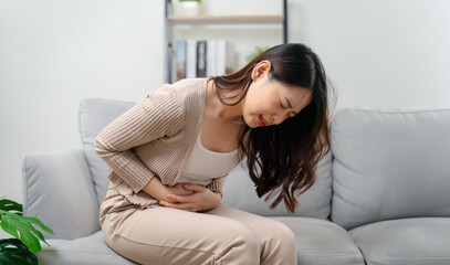 A woman is sitting on a couch holding her stomach with a stomach ache. Healthcare and medical.