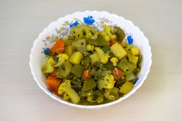 Healthy vegetables curry in a white ceramic bowl on a wooden surface, featuring a variety of mixed vegetables including cauliflower, carrots, beans, snake gourd, potatoes, pointed gourd, and cucumbers
