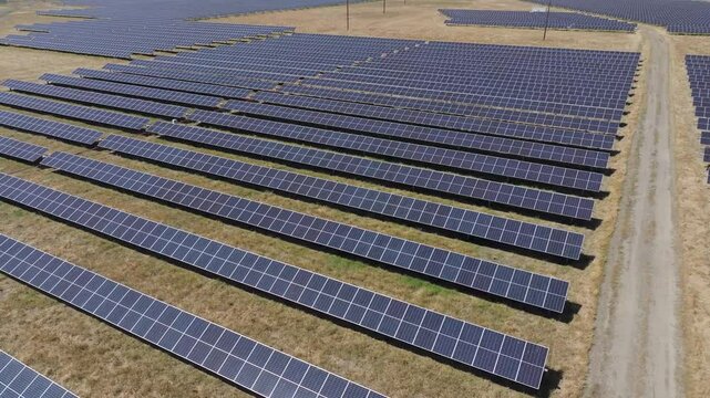 Aerial pan of solar panel rows in a barren grass field