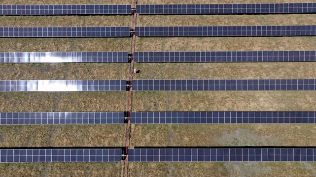 pulling up view on solar array row panels in barren grass field