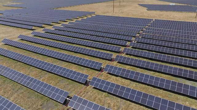 Aerial footage of solar panel rows in a barren grass field