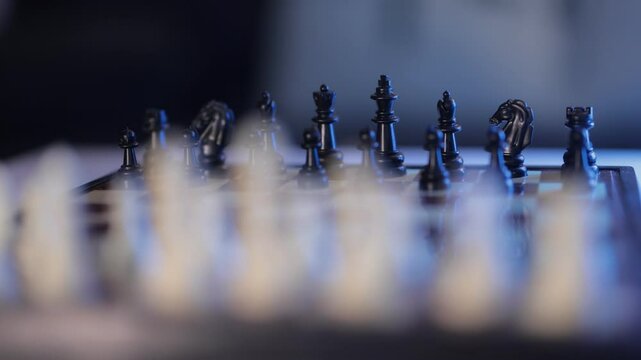 Slow motion video of chess game and board. Two rows of black and white figures of chess game at the beginning. Blue and white modern lighting.--