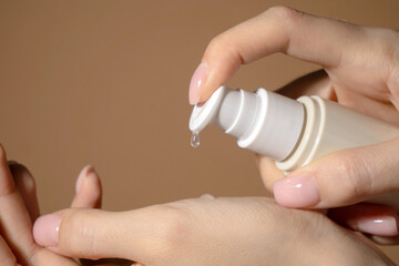 Drop of serum in close-up drips onto well-groomed female hand from an unmarked beige dispenser.