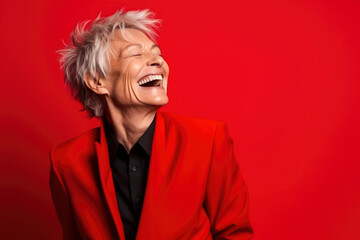 Gray-haired fashionable middle-aged woman in red jacket laughing with mouth wide open on solid red background. Businesswoman, modern elderly lady with short haircut. Creative woman