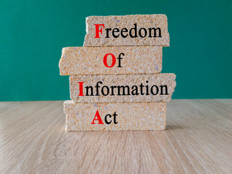 Brick blocks with words FOIA The Freedom of Information Act. Beautiful wooden table, green background. Business concept.
