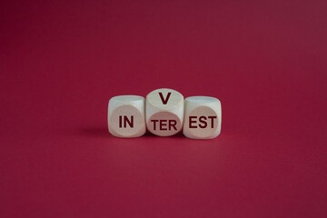 Invest or interest symbol. Turned wooden cubes and changes the word invest to interest. Beautiful red background. Business and invest or interest concept.