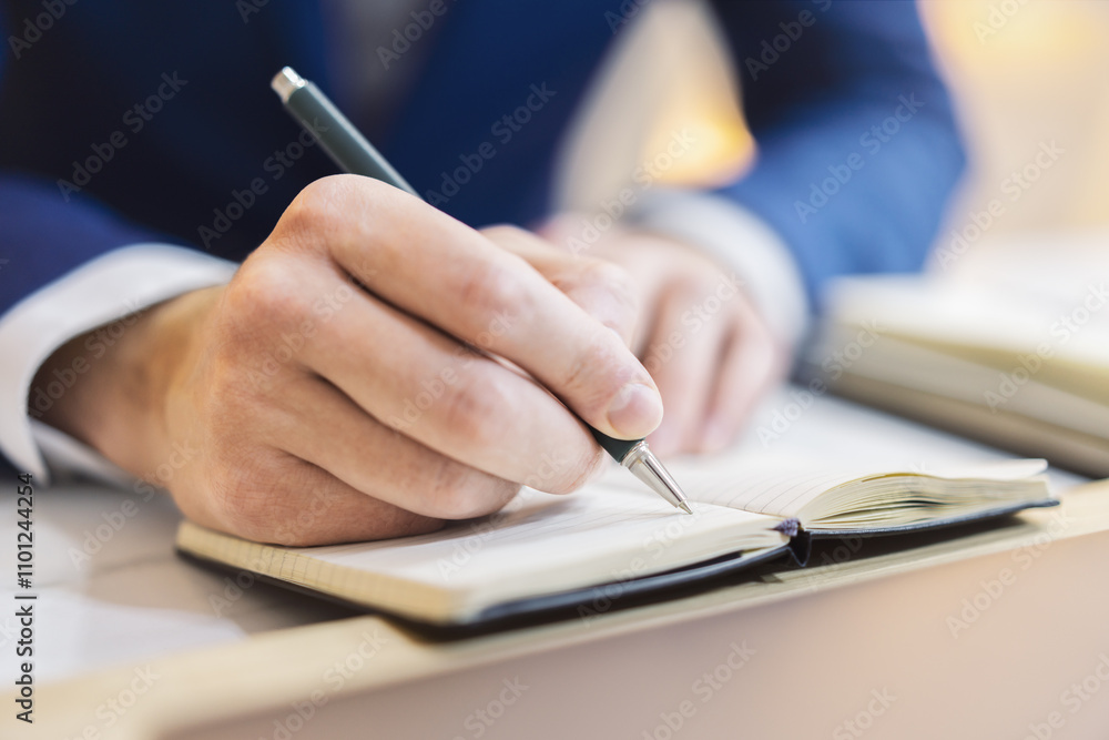 Aufkleber Close-up capture of a man's hand as he writes in a notepad, with an out-of-focus background
