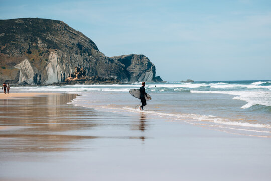Surfer walking towards waves with cliffs nearby in portugal