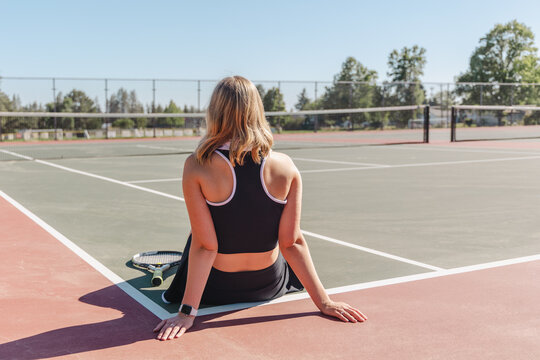 Tennis player sitting on the court, resting with a racket nearby