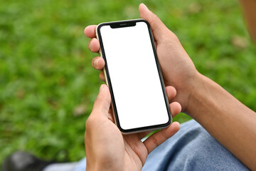 Close up of hands holding a smartphone with blank screen on background of green grass