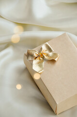 Minimalist Christmas Gift Box on Elegant White Fabric. Aesthetic Christmas composition with a beige gift box tied with a golden bow, resting on a white fabric background. Minimalist design perfect for